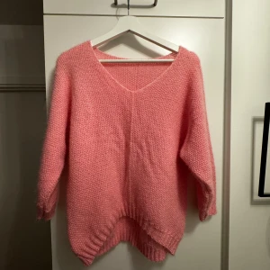 Rosa stickad tröja med v-ringning - Mysig rosa stickad tröja med v-ringning och långa ärmar. Perfekt för kyliga dagar med sin mjuka och bekväma passform. Ribbstickade muddar vid ärmslut och nederkant ger en fin detalj. Trekvartsärm.