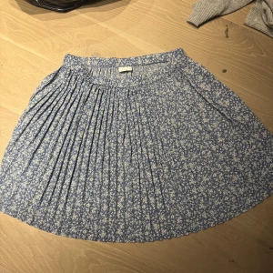 Kjol - Charmig blå kjol från Vila med ett sött blommönster i vitt. Kjolen har en plisserad design som ger en fin rörelse och volym. Perfekt för en somrig look!