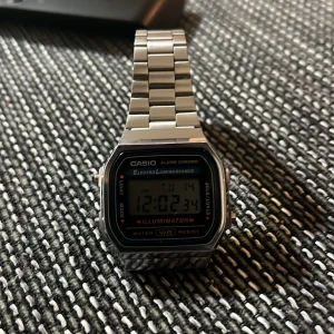 Casio digital klocka med stållänk - Säljer en klassisk Casio digital klocka med silverfärgad stållänk och rektangulär urtavla. Klockan har funktioner som alarm, belysning och stoppur. Perfekt för en retrostil! 🕒