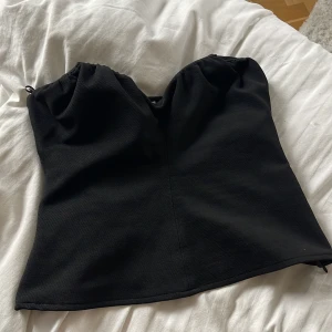 Svart axelbandslös topp - Snygg svart axelbandslös topp med en elegant passform. Perfekt för en kväll ute eller en speciell tillställning. 