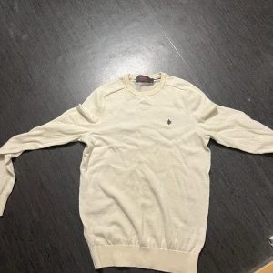 Vit tröja från Morris - Säljer en stilren vit tröja från Morris i storlek XS. Tröjan har en liten broderad detalj på bröstet och är tillverkad i mjukt material. Perfekt för en avslappnad och elegant look.