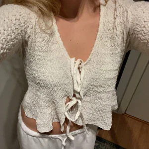 Vit ribbad kofta med knyt - Säljer en söt vit kofta med ribbad struktur och knyt framtill. Koftan har långa ärmar och en croppad design som ger en trendig look. 