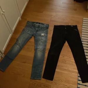 Två par jeans från Replay - Säljer två par Replay jeans. Ett par är ljusblå med slitningar och ett par är svarta. Båda har en slim passform och klassisk femficksdesign. Perfekta för en stilren look. 575 kr är priset för båda tillsammans. Det finns en liten söm slitning på fickan av dem svarta byxorna