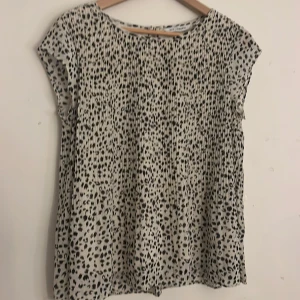 Mönstrad blus från KappAhl - Säljer en stilren blus från KappAhl i storlek S. Blusen har ett svart och vitt leopardmönster och korta ärmar. Den är tillverkad i ett lätt och luftigt material, perfekt för både vardag och fest. Baksidan har en liten öppning med knappdetalj.