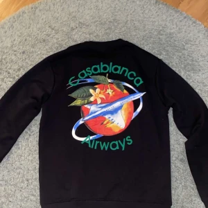 Svart sweatshirt från Casablanca - Snygg svart sweatshirt från Casablanca med ett färgglatt tryck av ett flygplan och texten 'Casablanca Airways' på ryggen. Framsidan har en mindre version av samma tryck. Perfekt för en avslappnad stil. Priset kan diskuteras vid snabb affär!!!