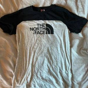 Grå och svart t-shirt från The North Face - Snygg t-shirt från The North Face i grått och svart. Den har korta ärmar och ett stort logotryck på framsidan. Perfekt för en avslappnad stil.