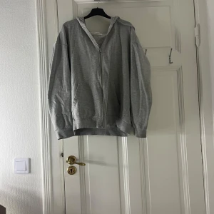 Grå hoodie från YOURTURN - Säljer en grå hoodie från YOURTURN med dragkedja och huva. Den har en avslappnad passform och är perfekt för kyligare dagar. Hoodien är tillverkad i ett mjukt material som känns skönt mot huden. Är även väldigt oversized och står ej storlek men skulle gissa på M
