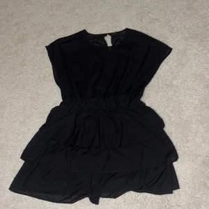 Svart klänning från Gina Tricot - Snygg svart klänning från Gina Tricot med volangdetaljer och prickigt mönster. Klänningen har en elastisk midja för en bekväm passform och är ärmlös, vilket gör den perfekt för varmare dagar.