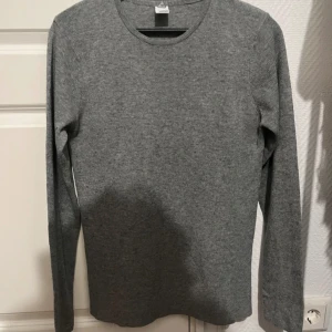 Grå långärmad tröja från Visual Clothing Project - Snygg och enkel grå långärmad tröja från Visual Clothing Project. Perfekt för en stilren och avslappnad look. Tröjan har en rund halsringning och är tillverkad i ett mjukt material.