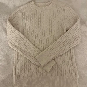 Beige stickad tröja - Säljer en stilren beige kabelstickad tröja med rund hals och långa ärmar. Ribbstickade muddar vid ärmslut och nederkant. Köpt på marknad för 499kr, aldrig använd. Storlek L/xl men passar M/L bättre. Vet ej märke men lapp syns på sista bild