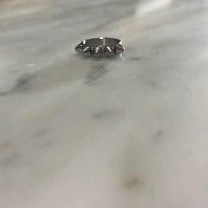 Silvrig ring med nitar - Cool silvrig ring med små nitar runtom. Perfekt för att ge en edgy touch till din stil. Passar bra till både vardag och speciella tillfällen.