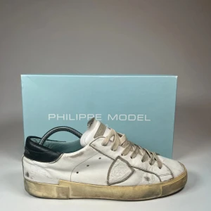 Philippe Model - Snygga vita sneakers från Philippe Model med klassisk design och snörning. Skorna har en smutsig look för en trendig stil och är tillverkade i skinn med en bekväm sula. Hör av er vid frågor eller funderingar!