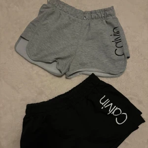 Grå och svarta shorts från Calvin Klein - Två par shorts från Calvin Klein i grått och svart. De har en elastisk midja och är perfekta för avslappnade dagar. Calvin Klein-loggan är tryckt på sidan. Passar både xs och s. 250kr för båda tillsammans!