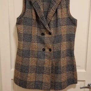 Rutig väst från Shein - Snygg rutig väst från Shein i jordnära färger. Västen har en dubbelknäppt design med svarta knappar och ett klassiskt mönster. Perfekt för att lägga till en stilfull touch till din outfit.