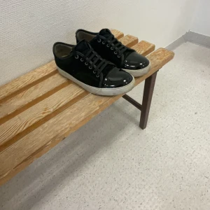 Svarta sneakers med glansig yta - Snygga svarta sneakers från Lanvin med en glansig yta och snörning. Skorna har en vit sula som ger en fin kontrast till det svarta. Perfekta för en stilren look. Storlek 42 passar 43. Uk8