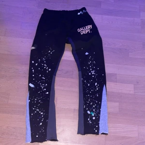 Svarta byxor från Gallery Dept. (pris diskuteras vid snabb affär) - Unika svarta byxor från Gallery Dept. med coola färgstänk och tryck. Byxorna har en elastisk midja och är perfekta för en avslappnad stil. De har en modern design med en konstnärlig touch.