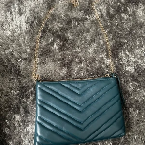 Blå quiltad axelväska med kedja - Snygg blå axelväska med quiltat mönster och guldfärgad kedja. Perfekt för att ge en stilren touch till din outfit. Väskan har en dragkedja för säker förvaring.