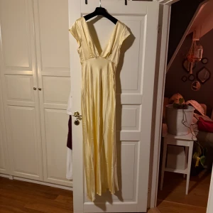 Gul långklänning med öppen rygg - Elegant gul långklänning i ett glänsande material med v-ringad design och öppen rygg. Perfekt för speciella tillfällen. Endast testad, skriv privat för fler bilder 💕