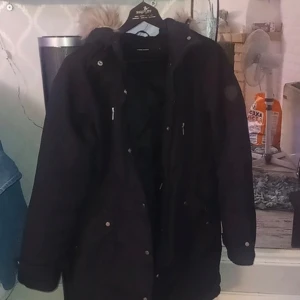 Svart jacka - Snygg svart parkajacka med avtagbar huva och pälsdetalj. Jackan har dragkedja och knappar framtill för extra skydd mot kyla. Perfekt för kalla säsonger. Har små hål vid fickan vid armen men det är inget som syns jätte mycket.
