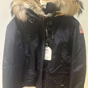Mörkblå jacka med pälsdetaljer från Parajumpers - Snygg mörkblå jacka från Parajumpers med pälsdetaljer på huvan. Jackan har dragkedja och flera praktiska fickor. Perfekt för kalla dagar med sin varma design och stilrena look.