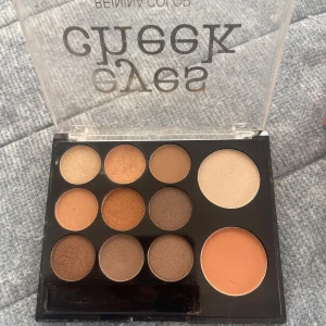 Ögonskuggspalett från Benina Color - Snygg ögonskuggspalett från Benina Color med 12 olika nyanser. Paletten innehåller både matta och skimrande färger i jordnära toner, perfekt för både vardag och fest. Den har en genomskinlig plastförpackning med texten 'eyes cheek' på locket. Är lite använt som det syns på bild och priset går att diskutera 