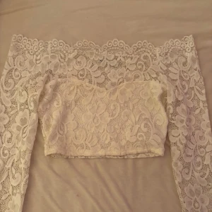 Vit spets topp från Nelly - Säljer en superfin vit spets topp från Nelly Toppen är offshoulder och croppad med långa ärmar. Perfekt sommartopp. Spetstoppen är i storlek S!✨Frakt ingår i priset 