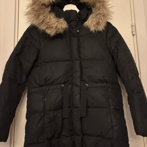 Svart dunjacka från Zara - Säljer en svart dunjacka från Zara med en mysig pälsfodrad huva. Jackan har långa ärmar och praktiska fickor med dragkedja. Perfekt för kalla vinterdagar. 🖤Har en ihop klistrad söm på baksidan vid armhålan men jag har aldrig tänkt på den förut. 