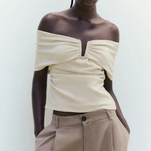 Beige offshoulder topp - Trendig beige offshoulder topp med rynkade detaljer och en elegant look. 