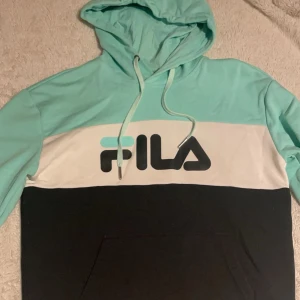 Turkos och svart hoodie från Fila - Snygg turkos och svart hoodie från Fila med vit detalj och logga på bröstet. 