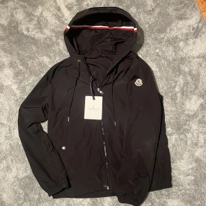 Moncler Grimpeurs Windbreaker  - Snygg svart vindjacka från Moncler med huva och dragkedja. Triangel och tags finns! NYSKICK! Använd 2 ggr så i princip ny. Hör av er vid frågor. Storlek 2 vilket motsvarar S/M. Billigare vid snabb affär!