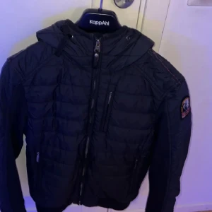 Svart jacka från Parajumpers - Säljer en svart jacka från Parajumpers i storlek XS. Jackan har en quiltad design med dragkedja och huva. Perfekt för kyligare dagar med sin fleecefoder. Nypris 3900 mitt pris 1500 kr, nyskick.