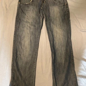 Jeans från G-Star RAW - Säljer ett par klassiska jeans från G-Star RAW i en snygg blå tvätt. De har en rak passform och är perfekta för en avslappnad stil. Jeansen har fem fickor och orange sömmar som ger en cool kontrast.