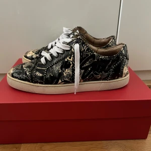 Mönstrade Christian Louboutin Sneakers - Snygga Christian Louboutin sneakers med unikt mönster i svart och beige i storlek 43. Skorna har den ikoniska röda sulan och vita snören. Perfekta för dig som vill sticka ut med stil de har släppt lite i lädret på sidan av den högra skorna vänligen se bild 4-5 för det. De är ingenting man ser när man använder skon på något sätt men därav priset. De är använda men sparsamt men har lite skavanker här och där. Skorna kommer utan låda. Hör av er om ni har några frågor :) 