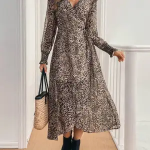 Snygg leopardmönstrad långklänning med v-ringning och volangdetaljer på axlarna. Klänningen har långa ärmar och ett knytband i midjan för en smickrande passform. Perfekt för en trendig look! Helt ny då returtiden till SHEIN gick ut.