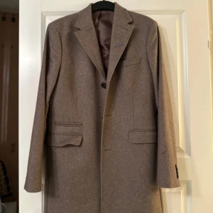 Beige kappa - Elegant beige kappa med klassisk design och knappar framtill. Perfekt för höst och vår, med långa ärmar och stilrena fickor. En tidlös jacka för en sofistikerad look. Kappan är från Riley i storlek 48.