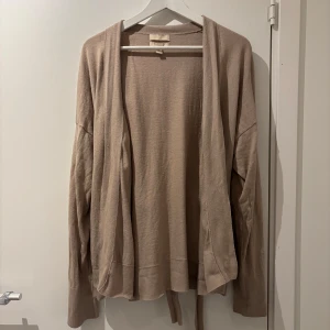 Beige kashmirblandad kofta från H&M - Säljer en elegant beige kofta från H&M i kashmirblandning. Koftan har långa ärmar och ett knytband i midjan för en stilren look. Perfekt för kyliga dagar och ger en lyxig känsla. Passar utmärkt till både vardag och mer uppklädda tillfällen.