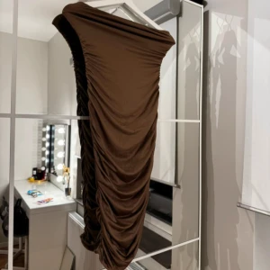 Brun offshoulder klänning - Elegant brun offshoulder klänning med rynkade detaljer längs sidorna. Perfekt för en stilfull kvällslook.