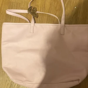 Rosa axelväska - Snygg rosa axelväska i syntetmaterial med enkel design. Perfekt för att bära med sig det nödvändigaste. Väskan har en stilren look och passar till många olika tillfällen.