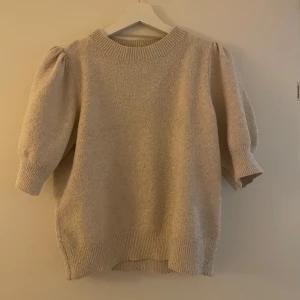 Beige stickad tröja med puffärmar - Mysig beige stickad tröja med puffiga trekvartsärmar och ribbade kanter. Perfekt för kyliga dagar och en stilren look.