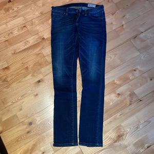 Mörkblå jeans från Crocker (Hit Low) - Snygga mörkblå jeans från Crocker (Hit Low) med en klassisk femficksdesign och låg midja. Jeansen har en dragkedja och knapp framtill. Perfekta för en avslappnad stil.