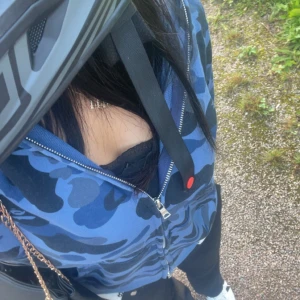 Blå camo hoodie från A Bathing Ape - Säljer en cool blå camo hoodie från A Bathing Ape. Den har en dragkedja och en unik hajdesign på huvan med färgglada bokstäver. Perfekt för att sticka ut i mängden! 🦈, den köptes här på plick