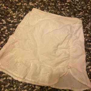 Vit kjol från H&M - Säljer en söt vit kjol från H&M med broderade detaljer och lite volangkant