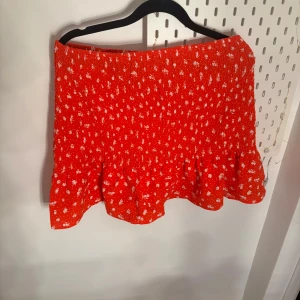 Röd blommig kjol - Säljer en söt röd kjol med blommigt mönster och volangdetaljer. Perfekt för en färgglad look. Kjolen har en kort längd och är lätt att matcha med olika toppar.