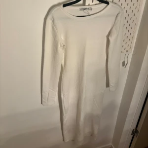 Vit ribbad klänning - Säljer en stilren vit ribbad klänning med lång ärm. Perfekt för en elegant och enkel look. Klänningen har en kroppsnära passform och är tillverkad i ett mjukt material som ger en bekväm känsla.