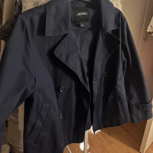 Mörkblå kappa från Monki - Snygg mörkblå kappa från Monki med dubbelknäppning och bred krage. Jackan har långa ärmar och två fickor framtill. Perfekt för en stilren look.