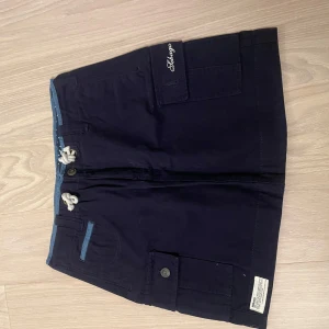 Mörkblå kjol  med fickor - Snygg mörkblå kjol med praktiska fickor och knappar. De har en knytning i midjan och en broderad detalj på ena fickan. Perfekta för en avslappnad stil.