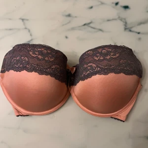Rosa och svart spets-bh - Snygg rosa bh med svarta spetsdetaljer och vadderade kupor för extra stöd. Perfekt för att bära under klänningar eller toppar med bara axlar.