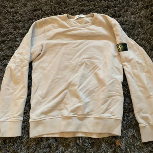 Beige tröja från Stone Island - Säljer en stilren beige tröja från Stone Island. Tröjan har långa ärmar och en rund halsringning. Den ikoniska Stone Island-loggan sitter på ärmen. Perfekt för en avslappnad och trendig look. Storlek 156 men passar mer 165 skulle jag säga.
