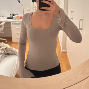 Beige långärmad topp - Säljer en stilren beige långärmad topp med en djup rund halsringning. Perfekt för lager-på-lager eller att bära som den är. Passar till både jeans och kjol för en avslappnad look.