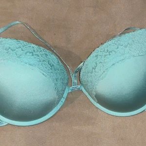 Turkos spets-bh med strassdetaljer - Snygg turkos bh med spetsdetaljer och strass på banden. Den har en elegant design med justerbara axelband och hakknäppning bak. Perfekt för att lägga till lite glamour i vardagen. Lite i strassen har försvunnit men inget som syns så tydligt